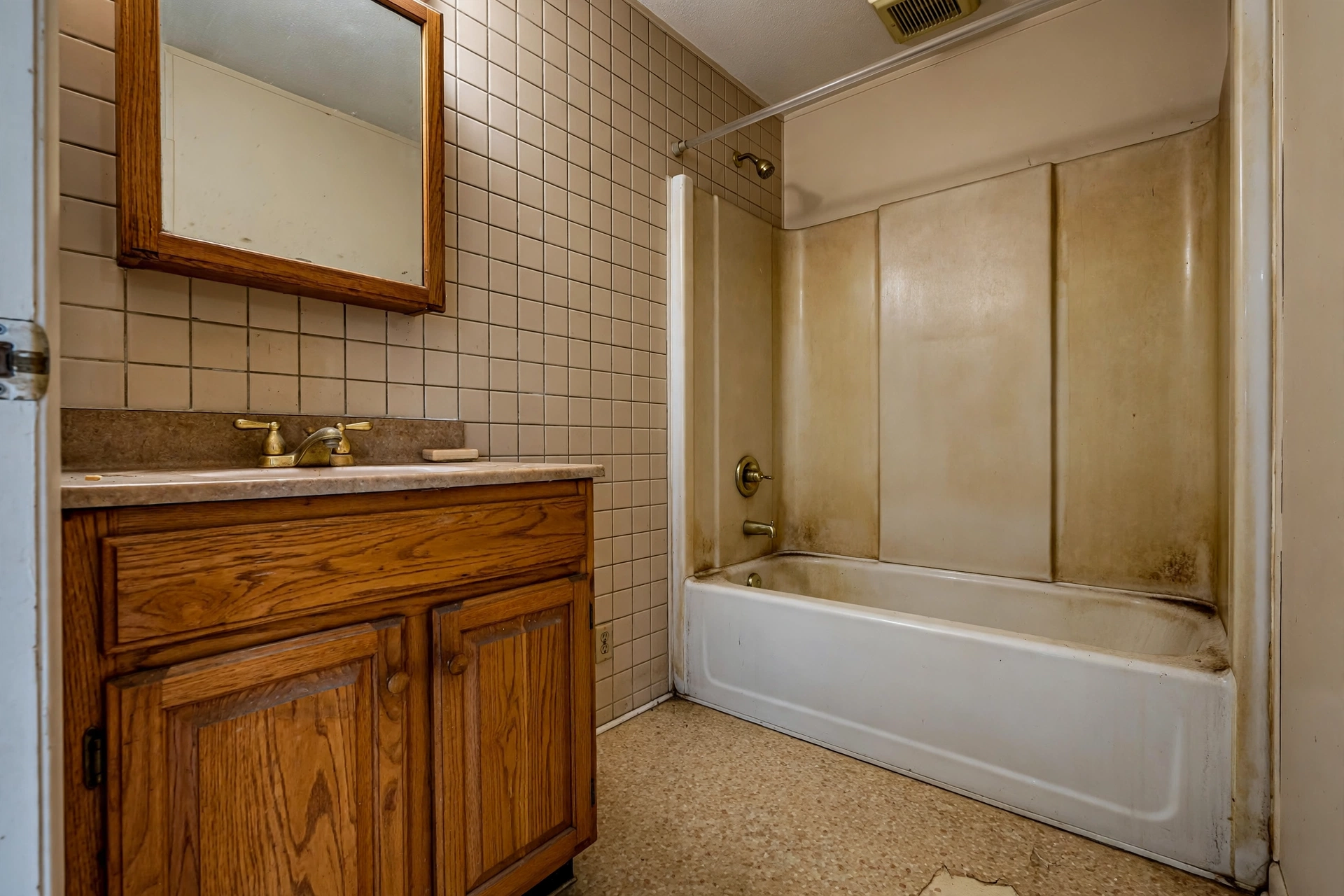 Dated 1990s Naperville hall bathroom before remodeling — oak vanity, stained tub surround, brass fixtures