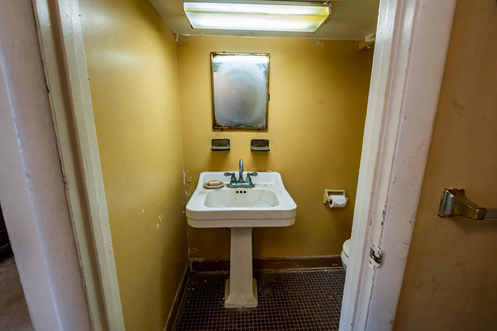 Tiny dated Naperville powder room with corroded pedestal sink and stained walls before remodeling